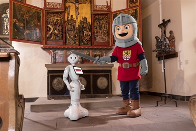 In den Museen der Burg Altena erhält Roboter-Dame Lüdia von Ritter Otto den Ritterschlag in Heimatkunde. Weitere Highlights des Erlebnistickets sind das AquaMagis in Plettenberg, die Dechenhöhle mit dem Deutschen Höhlenmuseum, die Phänomenta in Lüdenscheid, der Erlebnisaufzug zur Burg Altena sowie das Deutsche Drahtmuseum. Foto: Michael Bahr/Märkischer Kreis  